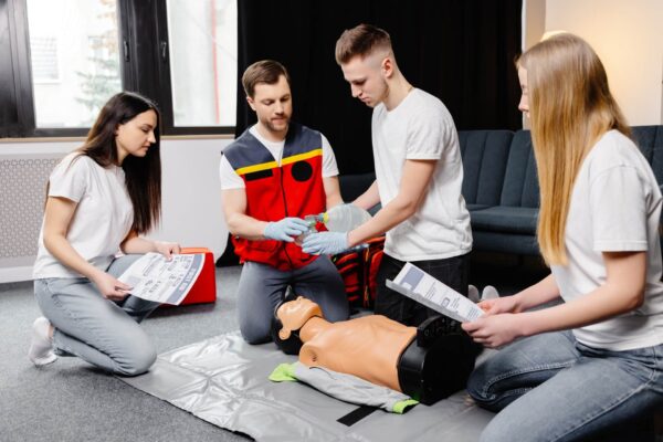 A first aid trainer with two women and one man practicing CPR on a dummy.