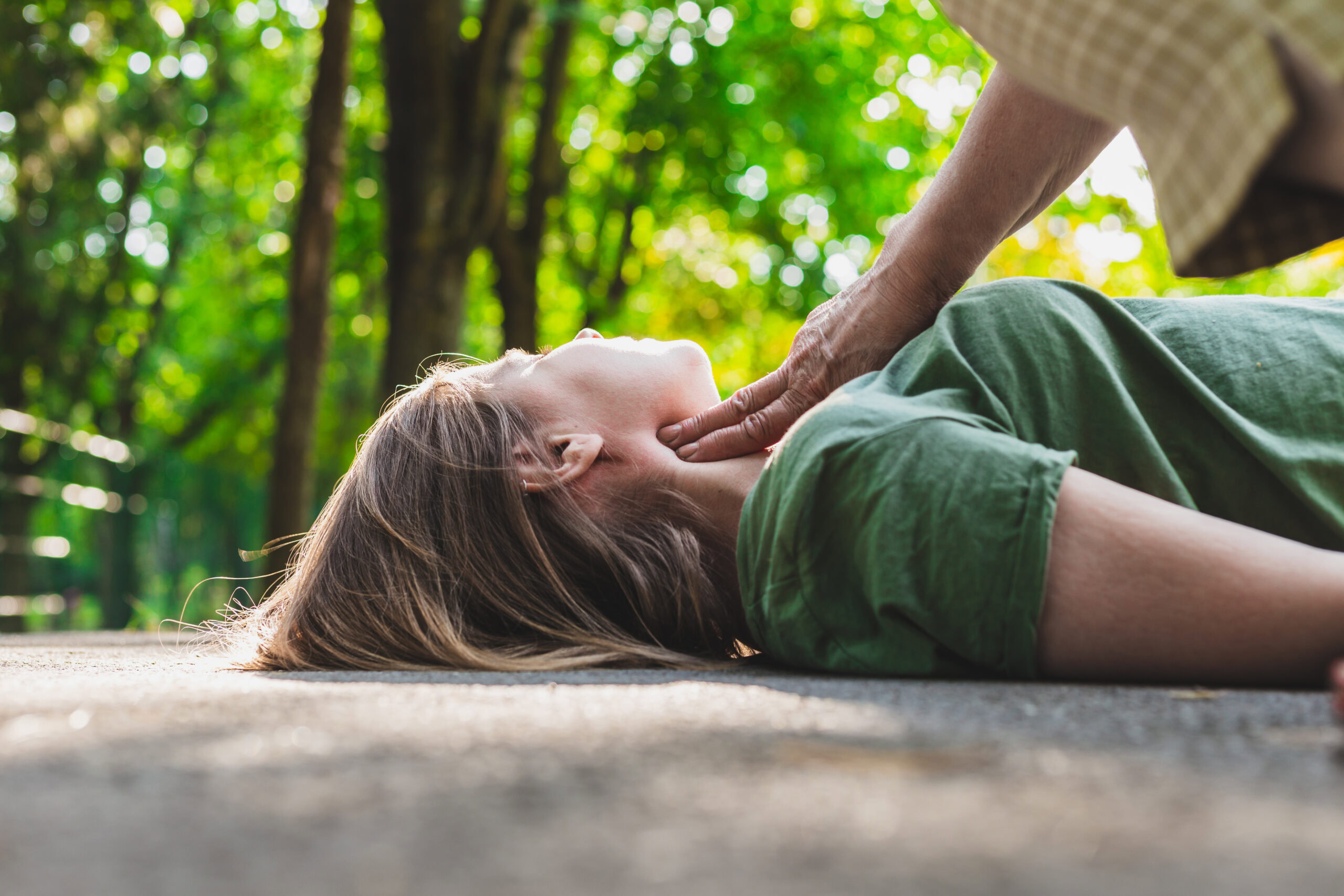 Unconscious fainted girl having pulse checked by an old woman – Teenager lying on the ground while her pulse is verified by an elder citizen on teen’s carotid artery